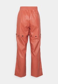 Orange faux leather pants with a loose fit, elastic waistband, and snap button detailing at the cuffs. Smooth texture and wide legs.