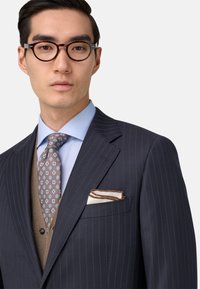 Jūras kara flotes striķu žakete ar gaiši zilu krekliņu, brūnu rakstu kaklasaiti un baltu kabatas lakatu ar brūnām svītrām. Apaļas bruņurupuča rāmja brillēm.