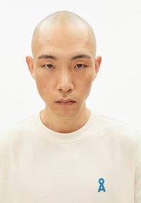 Katoenen sweatshirt in lichtcrème met een ronde hals, voorzien van een klein blauw logo op het linkerborstgebied. Soepele textuur, eenvoudig ontwerp.