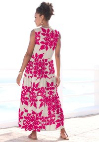 Maxikleid in hellbeige mit großen rosa Blumenmustern. Ärmelloses Design mit gestuftem Silhouette und lockerer Passform, getragen mit Sandalen.