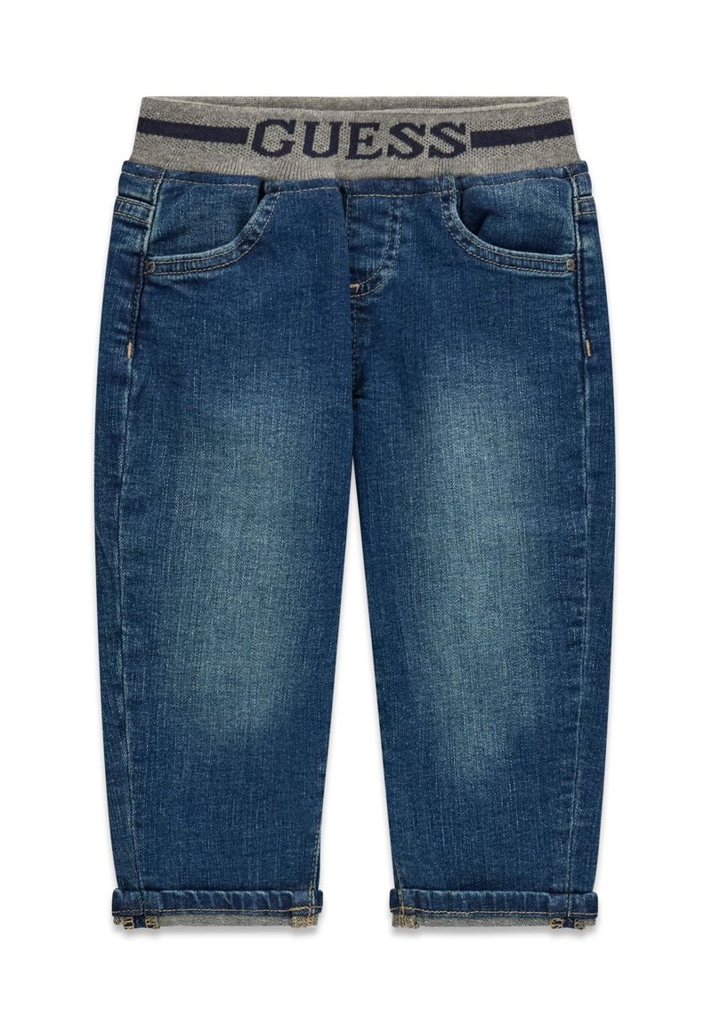 Jean en denim bleu foncé avec une ceinture élastique grise portant l'inscription "GUESS" en bleu marine. Comprend des poches avant et des ourlets retroussés.