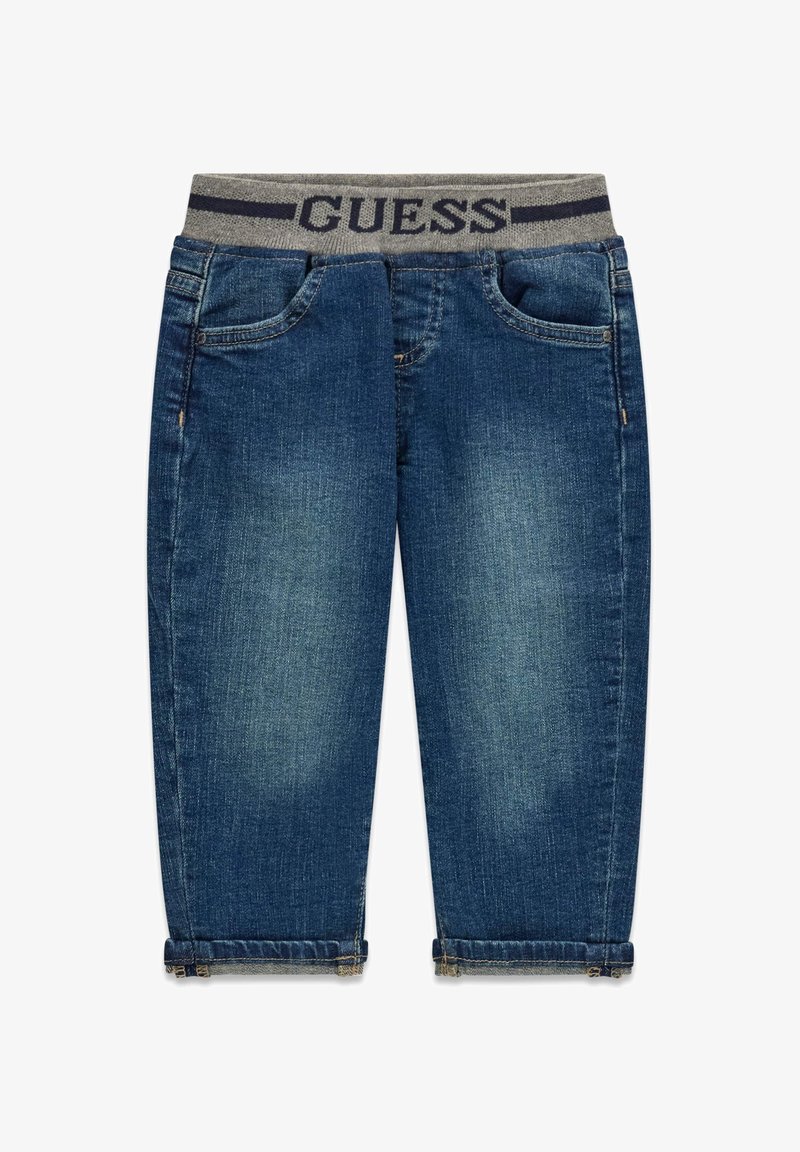 Jean en denim bleu foncé avec une ceinture élastique grise portant l'inscription "GUESS" en bleu marine. Comprend des poches avant et des ourlets retroussés.