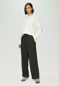 Weiße Bluse mit langen Ärmeln und Ausschnitt am Hals, kombiniert mit hoch taillierten dunklen Hosen und schwarzen offenen High Heels. Glatte Texturen und taillierte Passform.