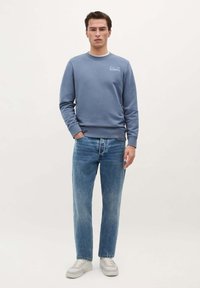 Lichtblauwe sweatshirt met ronde hals, geribde manchetten en logo op de borst, gecombineerd met lichtblauwe rechte jeans en witte sneakers.