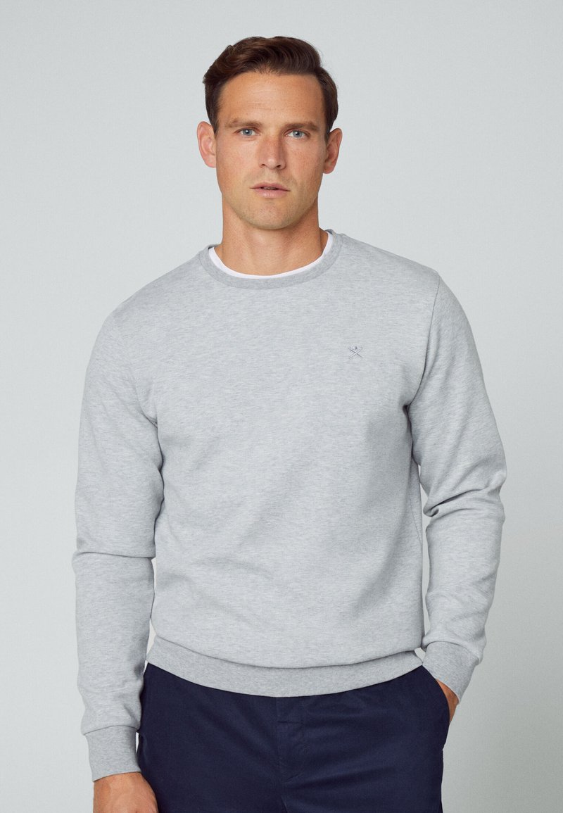 Hellgrauer Pullover mit Rundhalsausschnitt und langen Ärmeln, versehen mit einem dezenten Logo auf der Brust sowie gerippten Bündchen und Saum.
