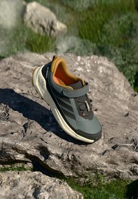 Szare buty trekkingowe z czarnym noskiem, pomarańczowym wykończeniem i zapięciem na rzep. Posiadają teksturowane akcenty oraz trzy czarne paski po bokach.