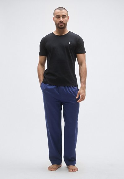 Črna kratka majica s kratkimi rokavi in modre sproščene hlače, obe iz mehkega materiala; majica ima majhen logotip na prsih.