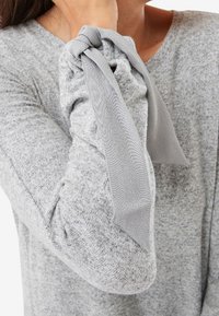 Top gris de manga larga con una tela texturizada, que presenta un acabado de manga fruncida con un detalle de cintas grises anudadas.