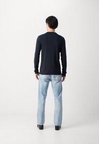 Marineblå langermet skjorte med rund hals, laget av mykt stoff. Kombinert med lyseblå rette jeans og svarte sko, sett fra ryggen.