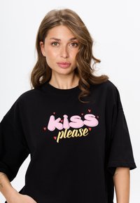 Czarny oversize T-shirt z wielokolorową grafiką, na której widnieje napis "proszę, pocałuj" w różowym i złotym, z małymi serduszkami.