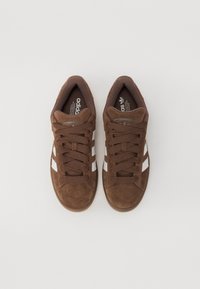 Brown suede sneakers with white stripes, rounded toe, and brown laces. Features a cushioned interior and textured sole for grip.