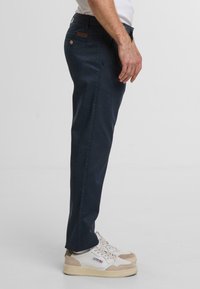 Granatowe chinosy o wąskim kroju, z materiału mieszanki bawełny, pięć kieszeni, oraz brązowa skórzana naszywka na plecach w talii.