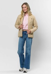 Bēša pūkainā jaka ar quilted dizainu, vilkta virs gaiši rozā krekla. Saskaņota ar ziliem platām biksēm un pelēkiem sporta apaviem.