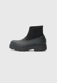 Bottes de cheville noires imperméables avec une semelle en caoutchouc et un dessus en tissu. Présente une semelle épaisse avec des crans de traction et un côté élastiqué pour un enfiler facile.