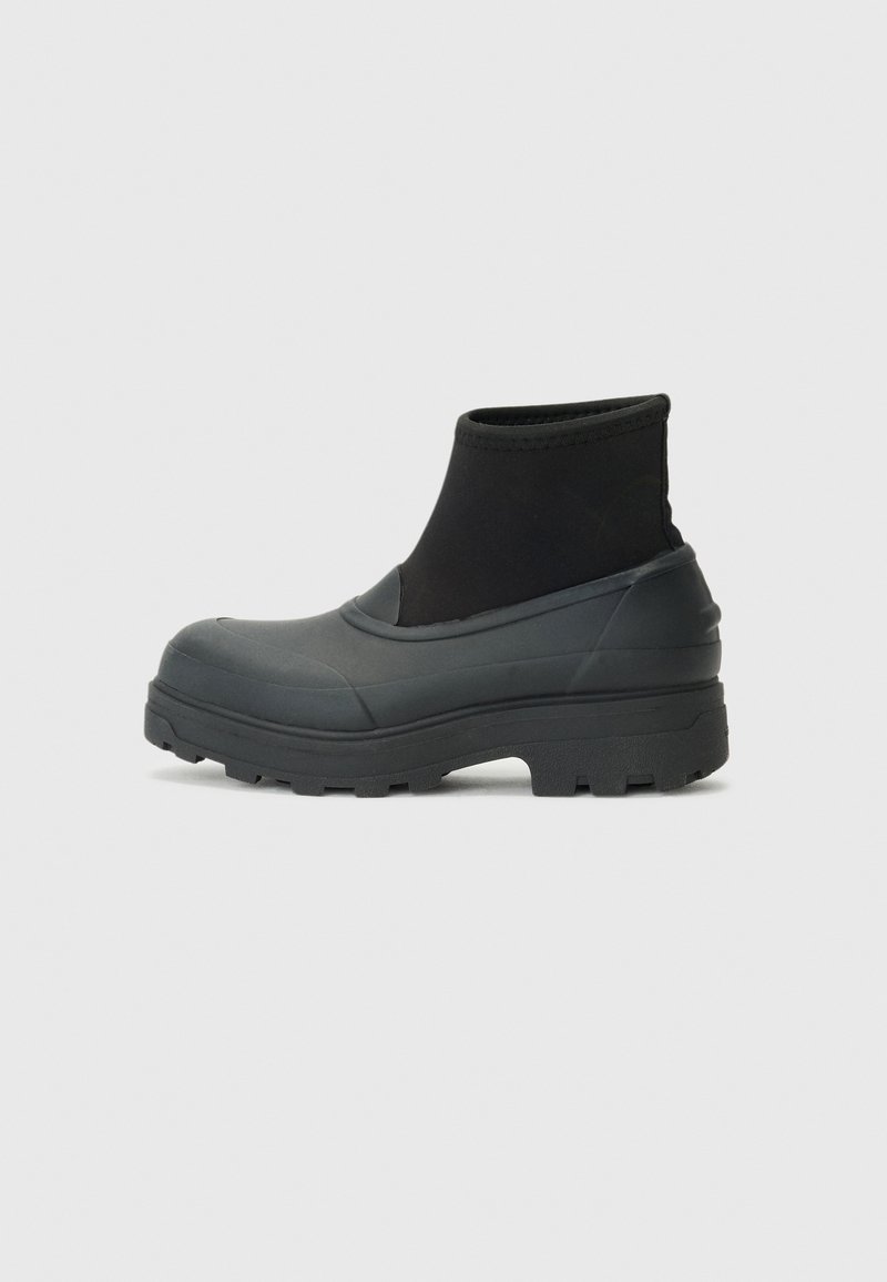 Bottes de cheville noires imperméables avec une semelle en caoutchouc et un dessus en tissu. Présente une semelle épaisse avec des crans de traction et un côté élastiqué pour un enfiler facile.