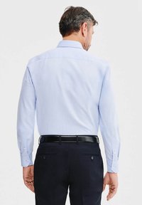 Jasnoniebieska koszula z długim rękawem i kołnierzykiem zapinanym na guziki, w połączeniu z ciemnymi spodniami i czarnym paskiem, widziana z tyłu.