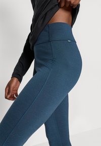 Wysokie legginsy w ciemnoniebieskim kolorze, wykonane z gładkiego, elastycznego materiału, z kontrastowym szwem i małym logo w pobliżu pasa.
