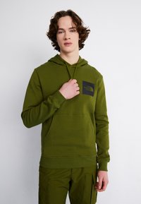 Felpa verde con cappuccio, dotata di tasca frontale e patch logo nero. Il tessuto sembra morbido; i polsini e il bordo in vita sono a costine per una vestibilità migliore.