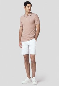 Jasnoróżowa koszulka polo z kołnierzykiem i subtelną fakturą, w połączeniu z białymi szortami. Strój dopełniają białe sneakersy.
