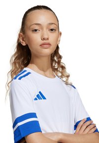 Maillot de sport blanc avec des rayures bleues sur les manches et les épaules. Présente un logo bleu, un col rond et des manches courtes. Texture de tissu douce.