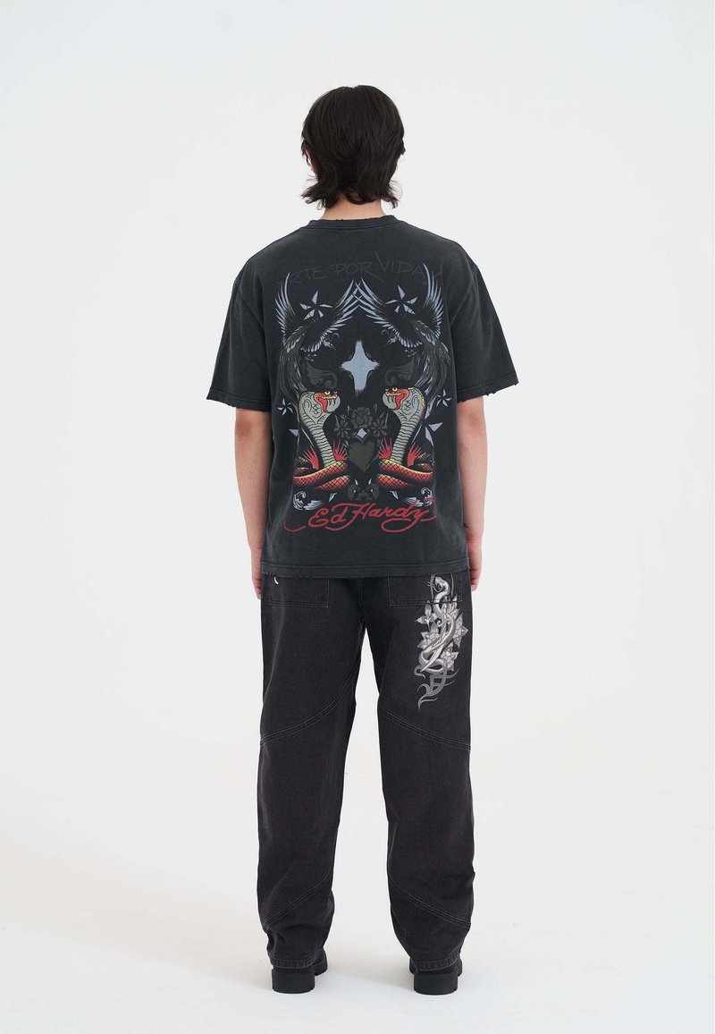 Sort grafisk t-shirt med slange- og ørnedesign, med "Ed Hardy" tekst. Sammen med sorte denim bukser prydet med et sølv mønster.