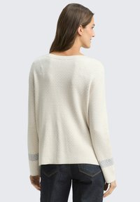 Maglione beige chiaro con motivo a maglia testurizzato, scollatura ampia e maniche lunghe con una banda grigia a contrasto sui polsini. Vista dal retro.