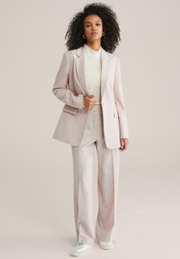 Jasnoróżowy, dopasowany garnitur o luźnym kroju, z marynarką zapinaną na jeden guzik i szerokimi spodniami. W zestawie z teksturowanym kremowym topem i białymi butami.