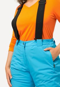 Blauwe skibroek met verstelbare zwarte banden, zijzak met rits en een gladde textuur, gecombineerd met een oranje langemouwen T-shirt.