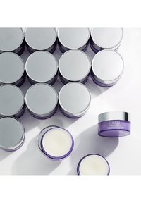 Contenants de crème Clinique ; couvercles en métal argenté avec des bases violettes. Un pot est ouvert, laissant voir une crème blanche. Entouré de pots similaires scellés.