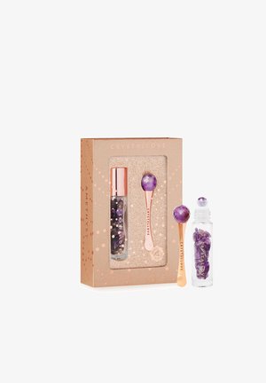 Zestaw kosmetyków z kryształem ametystu w pudełku z różowymi złotymi akcentami. Zawiera narzędzie do masażu oraz przezroczystą fiolkę wypełnioną kamieniami ametystu.