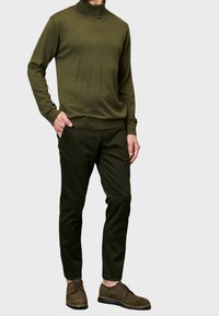 Pull en col roulé vert olive associé à un pantalon vert foncé fuselé et des chaussures en daim marron. Texture douce, poignets côtelés et taille côtelée.