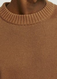 Brauner Strickpullover mit einem gerippten Ausschnitt, strukturiertem Stoff und klassischer runder Form. Nahaufnahme hebt die Nähdetails hervor.