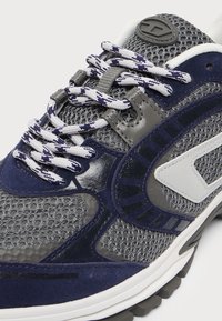Baskets gris et bleu marine avec des lacets blancs et bleu marine à motifs, tissu en mesh, détails en suède et cuir, et un logo blanc sur le côté.