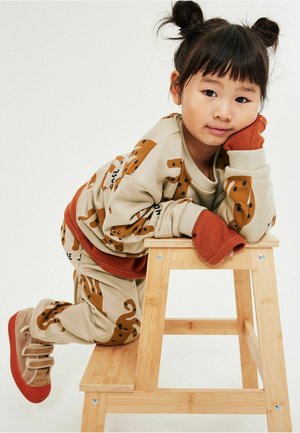 Beżowy komplet bluzy i spodni z zabawnym wzorem psa, z pomarańczowymi akcentami i ściągaczami. Dziecko ma na sobie brązowo-czerwone buty.