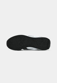 Talpă neagră din cauciuc cu un model de tread hexagonal al unei tenisi alb-negru, văzută de jos pe un fundal alb simplu.