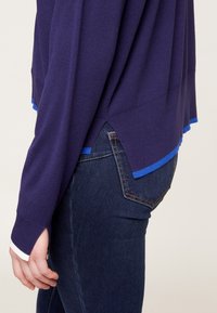 Marinblå tröja med vita och blå randiga detaljer vid ärmslut och nederkant, mjukt material, avslappnad passform och sidoflikar för bättre rörelsefrihet.