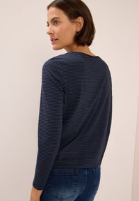 Chemise à manches longues rayée marine avec col rond, en tissu doux et coupe décontractée, associée à un jean bleu. Texture subtile des rayures visible.