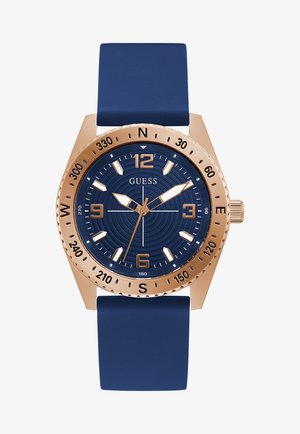 Montre avec bracelet en silicone bleu marine et boîtier en or rose. Le cadran rond présente un fond texturé bleu, des index horaires en or et des aiguilles.