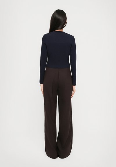 Pull en tricot côtelé bleu marine à manches longues associé à un pantalon marron ample à taille haute. Design simple, texture lisse, couleurs unies.