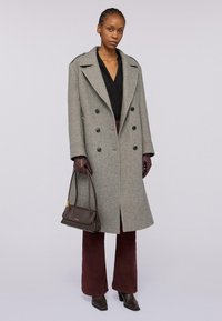 Šedý vlněný peacoat s dvouřadým zapínáním, velkým límcem a bočními kapsami, v kombinaci s hnědou koženou kabelkou a bordó širokými kalhotami.