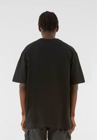 Sort oversized bomulds T-shirt med korte ærmer, rund halsudskæring og lige kant. Ingen synlige mønstre eller grafik på ryggen.