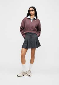 Μπορντό κοντό φούτερ με φερμουάρ, ανοιχτό μπλε πουκάμισο με γιακά από κάτω, γκρι φούστα με πιέτες και μπεζ αθλητικά με λευκές κάλτσες.