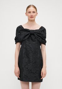 Čierne krátke šaty s textúrovaným kvetinovým vzorom, širokým off-shoulder mašľovým detailom, priliehavým strihom a hladkým materiálom.
