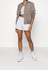 Khaki bomberjack met geribbelde manchetten, grijs crop top, licht denim short en witte hoge sneakers met grijze sokken. Eenvoudig ontwerp en pasvorm.