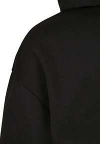 Gros plan d'un tissu tricoté noir montrant la texture détaillée et la couture sur l'épaule et la partie supérieure du dos d'un vêtement.