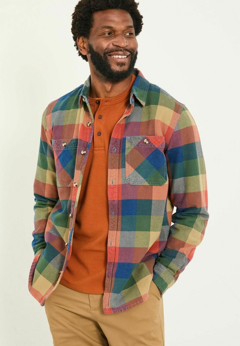 Mehrfarbige Karoshemd mit grünen, blauen, roten und gelben Quadraten; zwei Brusttaschen; darüber getragen ein rostfarbenes Henley-Shirt.