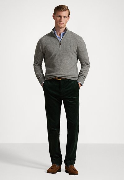 Grå lynlås sweater over en blå skjorte, parret med mørkegrønne corduroybukser og brune ruskindssko. Enkle, rene linjer og teksturer er synlige.