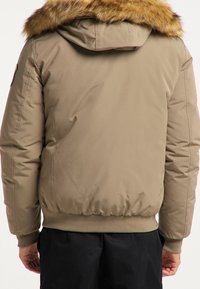 Giacca imbottita color nocciola con cappuccio foderato in pelliccia, polsini e vita a coste, e una superficie liscia. Presenta un design pratico senza hardware visibile.