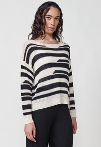 Pulover tricotat în dungi, crem și negru; decolteu larg, mâneci lungi, croială lejeră, tiv cu nervuri. Purtați cu pantaloni negri cu nervuri.