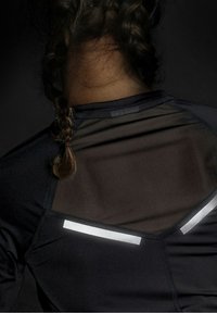 Top atletico nero con pannello posteriore in rete, dettagli riflettenti e vestibilità aderente. Include un collo alto e tessuto strutturato.